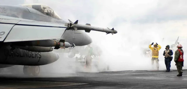 An AIM-9X Sidewinder on the wingtip of an F/A-18E Super Hornet on an aircraft carrier catapult