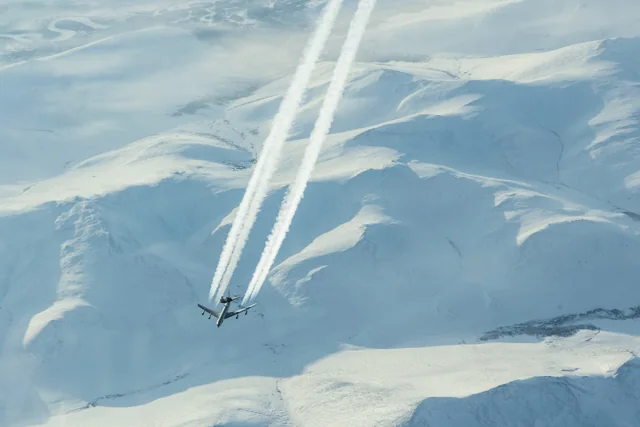 A U.S. Air Force E-3 Sentry leaving contrails above snowy Arctic mountains