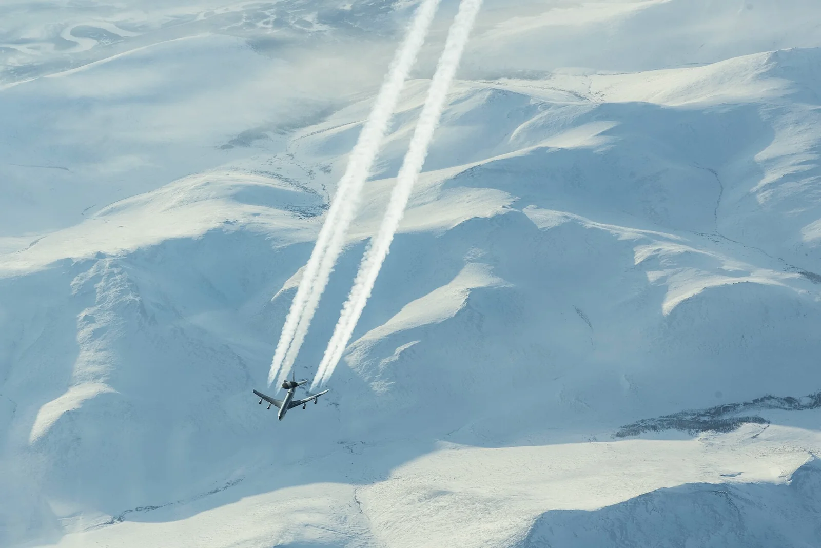 A U.S. Air Force E-3 Sentry leaving contrails above snowy Arctic mountains