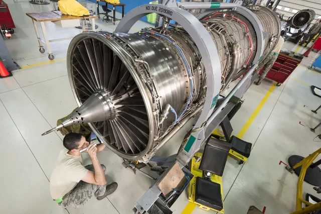 A Pratt & Whitney F100-PW-229 engine on a maintenance stand at RAF Lakenheath, with an airman inspecting the fan