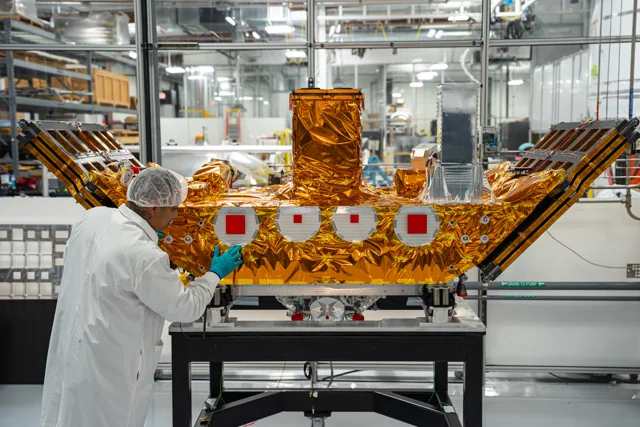 An engineer working on the gold-blanketed Impulse Space Mira spacecraft in a cleanroom