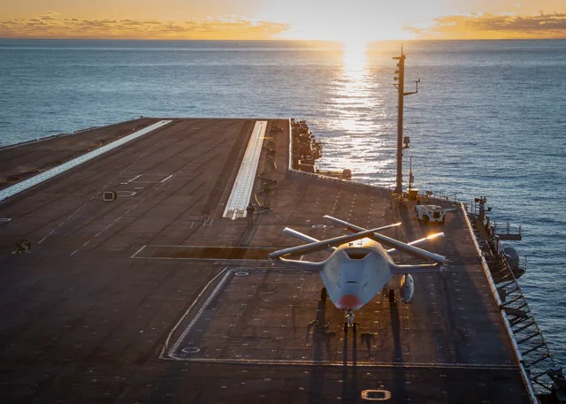 An MQ-25 test aircraft on the flight deck of USS George H.W. Bush at sunset.