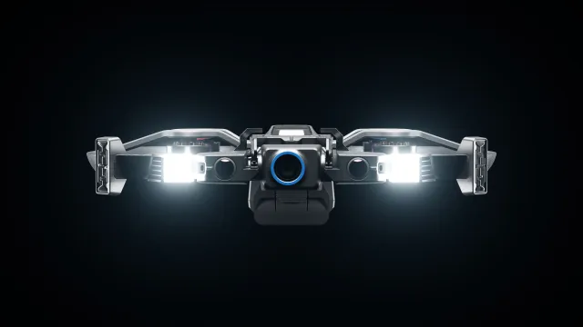 Skydio R10 product image, front view with protective frame, camera, and lights against a dark background.